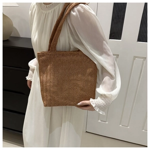 Detail of woven straw tote bag texture and long handles worn by a model in a minimal room