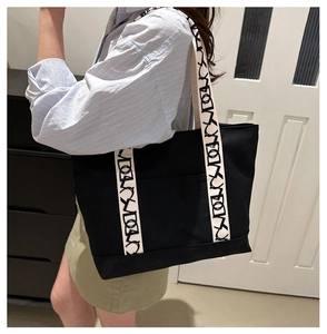 Détail d'un grand sac fourre-tout noir en toile avec bandoulière crème à motifs