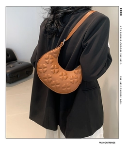 Detailed view of the brown crescent bag featuring embossed clover textures and silver hardware