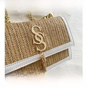 Detail of woven straw flap bag with white leather trim and gold letter metal lock