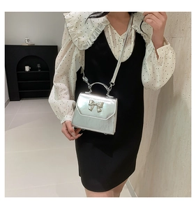 Detail of silver metallic crossbody bag with stylish bow accent and mirror finish