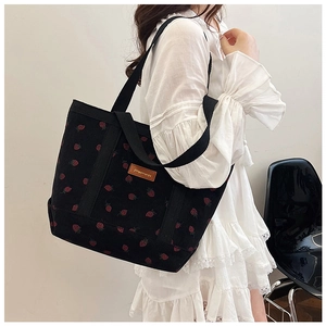 Detail of black corduroy tote bag featuring red strawberry patterns and top handles