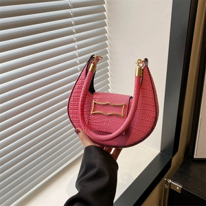 Pink croc-embossed crescent handbag with gold buckle shown in a handheld lifestyle shot