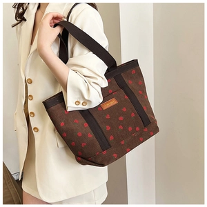 Detail of brown corduroy tote bag featuring red strawberry prints and leather brand tag