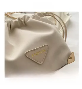 Detail of cream drawstring bucket bag showing gold logo plaque and metallic chain strap