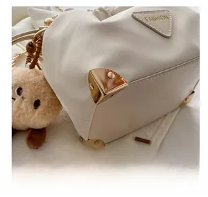 Detail of white bucket bag with golden metal corners and cute bear pendant charm