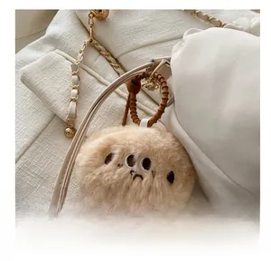 Close-up of a brown plush charm with sad face embroidery on a white crossbody bag