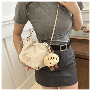 Detail of white drawstring bucket bag with gold accents and cute plush charm pendant