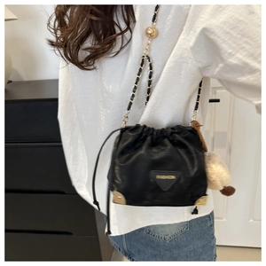 Detail of black drawstring bucket bag with gold chain strap and plush pompom charm