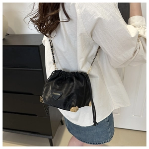 Detail of black drawstring bucket bag with gold corners and chain shoulder strap