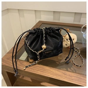 Detail of black drawstring bucket bag with gold metal corners and chain strap on a glass table