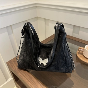 Sac à épaule plissé noir chic avec boucle papillon argentée sur une table en bois