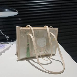 Chic off-white tote bag with floral embroidery and tassel on a white table top
