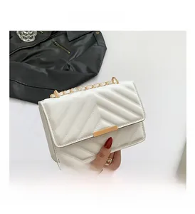 Detail of white quilted crossbody bag featuring a gold clasp and elegant chain strap