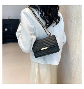 Detail of black quilted shoulder bag with golden chain strap and chevron stitching pattern