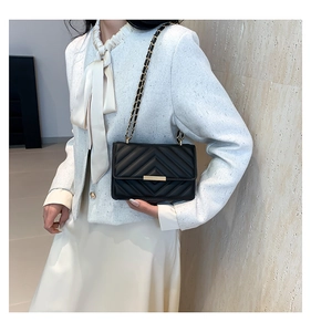 Close-up of elegant black quilted leather shoulder bag with gold hardware on model