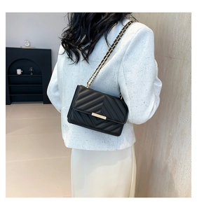 Detail of black chevron quilted crossbody bag with gold chain strap worn by a model