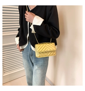 Detailed close-up of a gold quilted crossbody bag with a metallic chain strap on a model