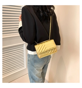Detail of gold V-quilted faux leather crossbody bag with elegant chain strap and metallic finish