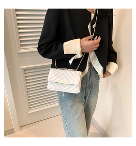 Close-up of a white quilted leather flap bag with gold metal bar and chain strap detail