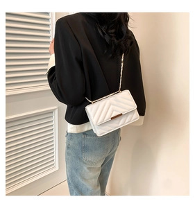 Detail of white quilted crossbody bag featuring V-shape stitching and gold chain strap