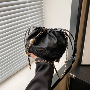Black drawstring bucket bag with gold chain strap and metal corner accents in hand