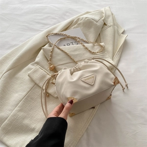 Chic off-white drawstring bucket bag with gold chain strap on a blazer background