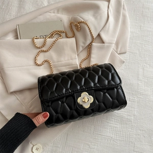 Quilted black chain bag with clover gold lock on a beige blazer background