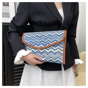 Detail of hand-held straw clutch with blue and white stripes and brown leather trim