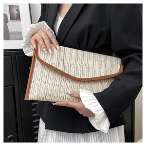 Detail view of a beige straw woven envelope clutch with brown leather trim held by a model
