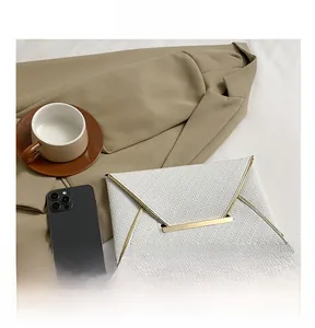 Gros plan d'une pochette enveloppe blanche en similicuir tissé avec bordure dorée