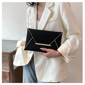 Detail of elegant black envelope clutch bag featuring gold metal trim and textured finish