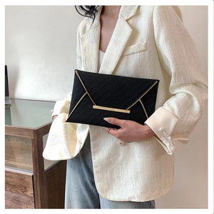 Close-up of black envelope clutch bag featuring refined gold metal edge and textured finish