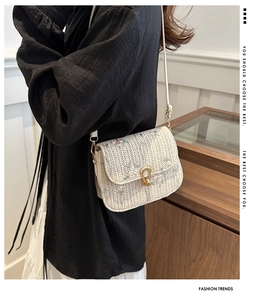 Detail of floral embroidery and metallic horseshoe lock on straw crossbody saddle bag