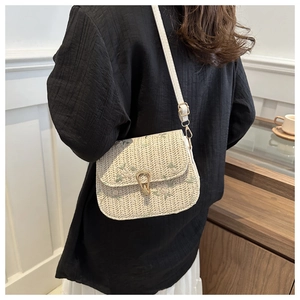 Detail of floral embroidery and gold metal buckle on a woven straw saddle bag
