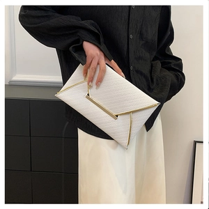Close-up of white woven envelope clutch bag with elegant gold metal trim held by a model