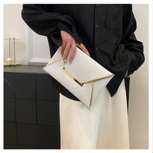 Detail view of a white envelope clutch with woven texture and elegant gold metal trim