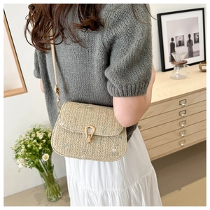 Detail of beige woven saddle bag with floral embroidery and gold metal clasp