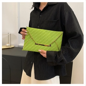 Détail macro d'une pochette enveloppe tissée vert vif avec garnitures métalliques dorées