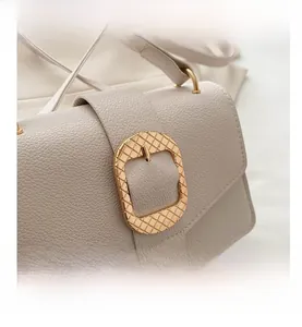 Close-up of beige lychee grain leather handbag with textured golden square buckle detail