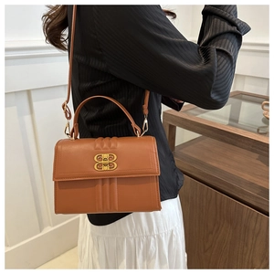 Sac à main en cuir marron avec boucle dorée et coutures verticales porté par un mannequin