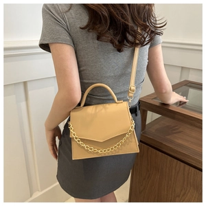 Detail of light tan crossbody bag with gold chain strap and textured flap closure