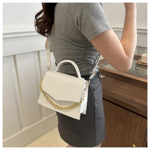 Close-up of a white crocodile embossed leather crossbody bag with a gold metal chain strap