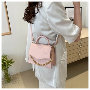 Detail of pink crossbody bag featuring croc texture and gold chain on white blazer
