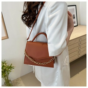 Detail of a brown leather bag with crocodile texture and decorative gold chain strap