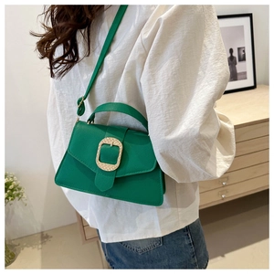 Green leather handbag with gold buckle shown on model in a modern home interior