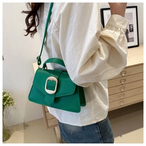 Close-up of a green leather bag with gold buckle on a model in a cozy interior
