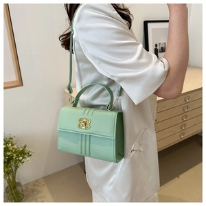 Détail du sac bandoulière vert menthe avec boucle dorée en B sur une tenue crème