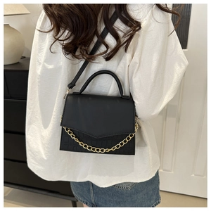 Close-up of black faux crocodile skin handbag with gold chain detail on white outfit