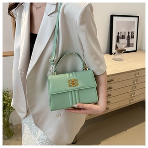 Détail du sac à bandoulière vert menthe avec boucle dorée en B et costume blanc chic